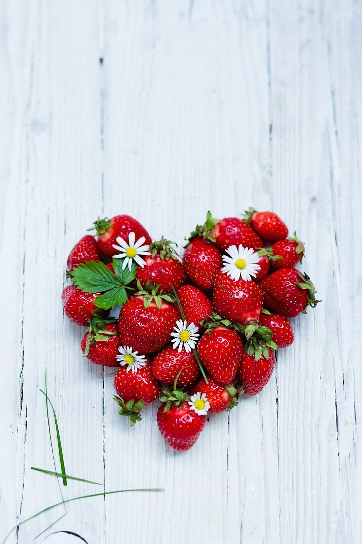 Ein Herz aus frischen Erdbeeren auf weißem Holzuntergrund