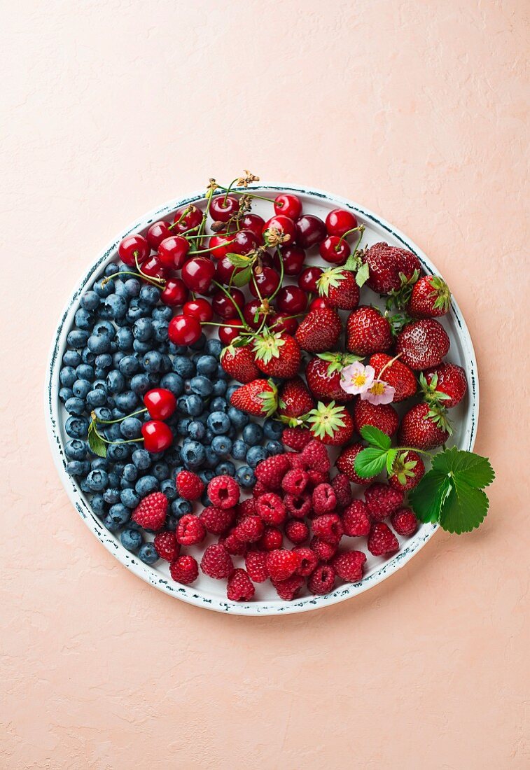 Fresh berries and cherries on a plate on a coloured surface