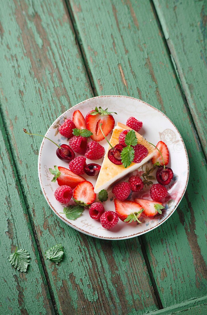 A slice of cheesecake with fresh berries on a green wooden surface (seen from above)
