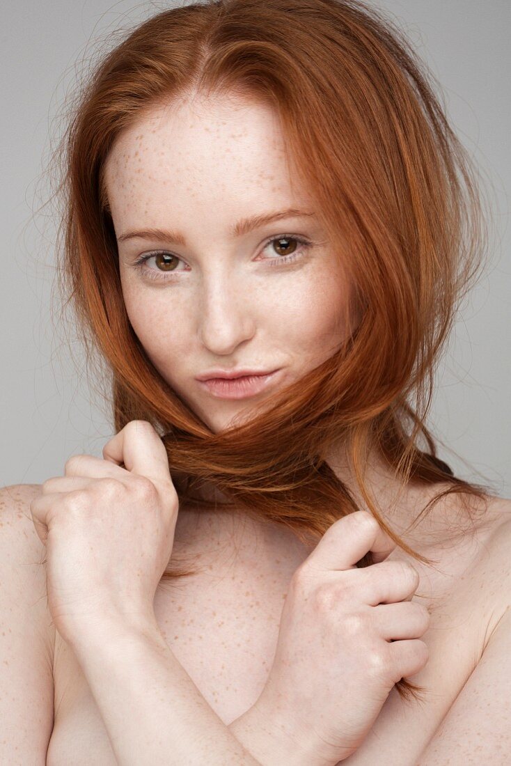 Portrait einer jungen Frau, die mit ihren roten Haaren spielt