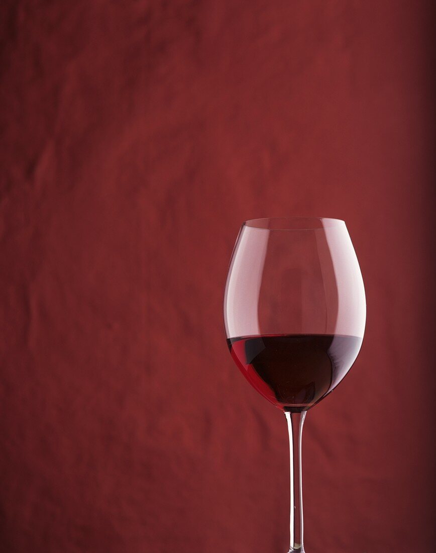 A filled red wine glass against red background