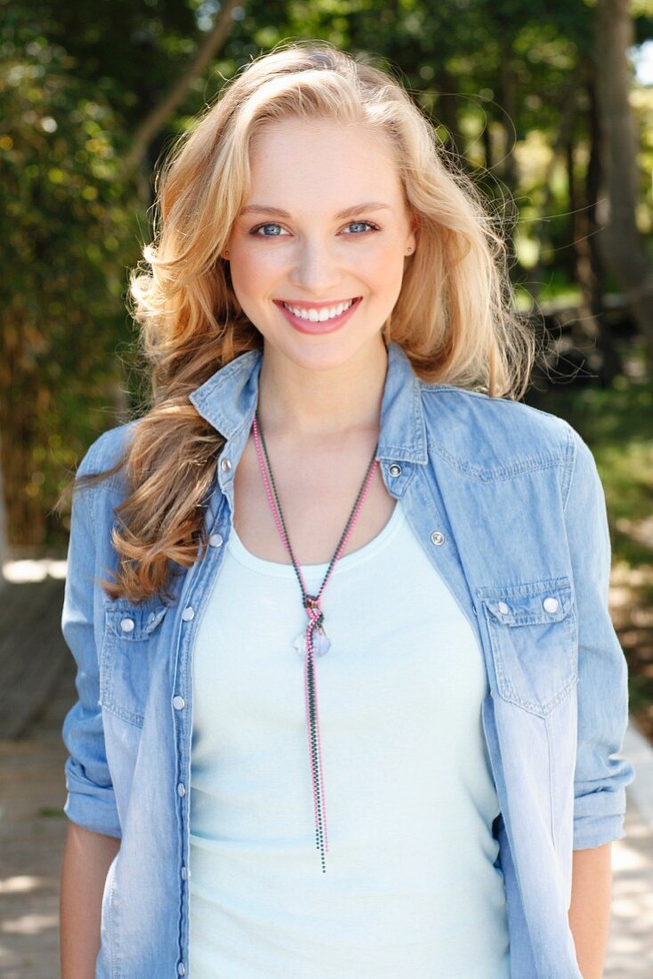 A young blonde woman wearing a light top and a denim blouse