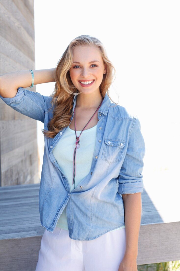 A young blonde woman wearing a light top, trousers and a denim blouse