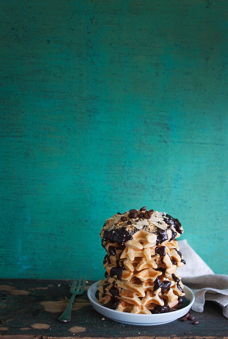 A stack of waffles with a chocolate and coffee sauce, almonds and hazelnuts