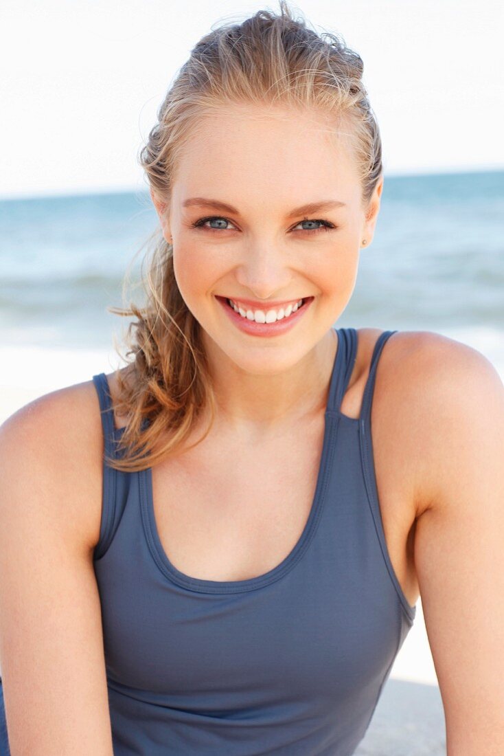 A young dark blonde woman on a beach wearing a purple tank top