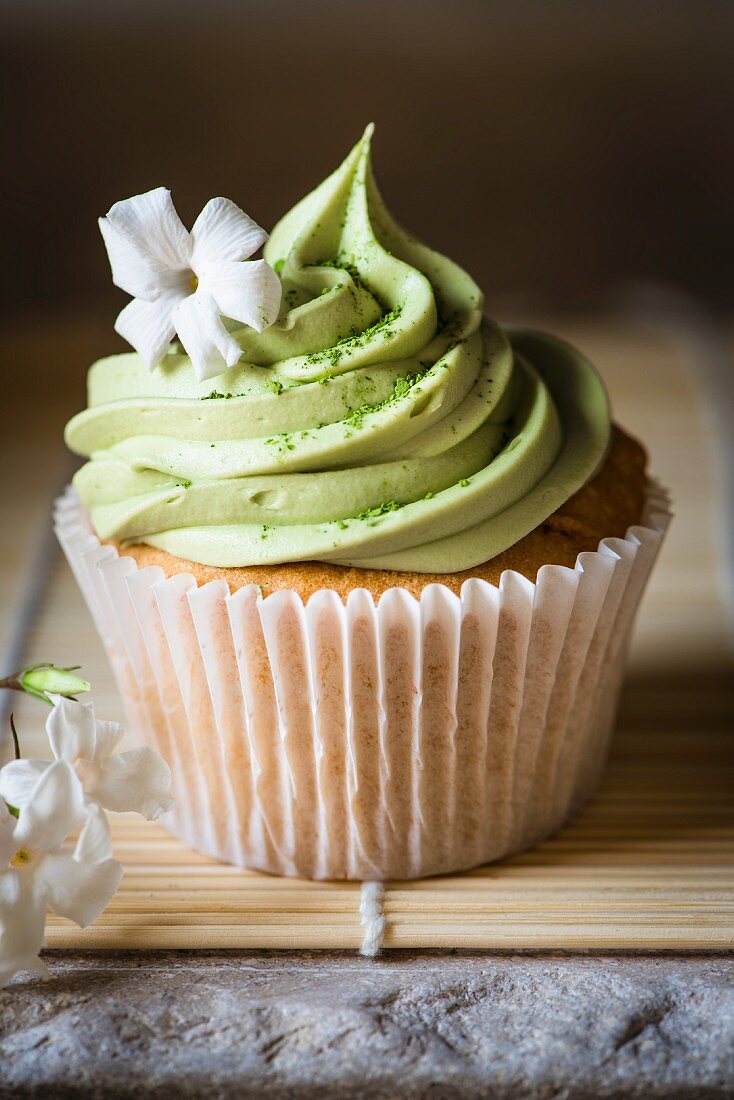 A cupcake with matcha frosting and a jasmine flower