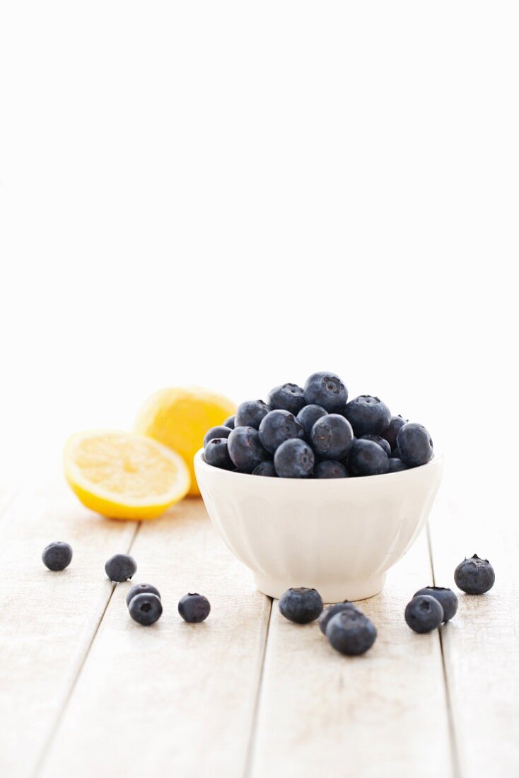 A bowl of fresh blueberries with lemon in the background