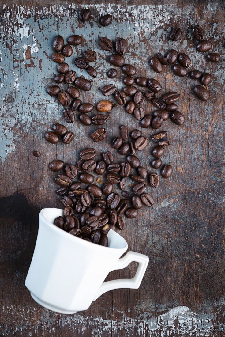 Coffee beans scattered over a rustic surface with a white coffee cup