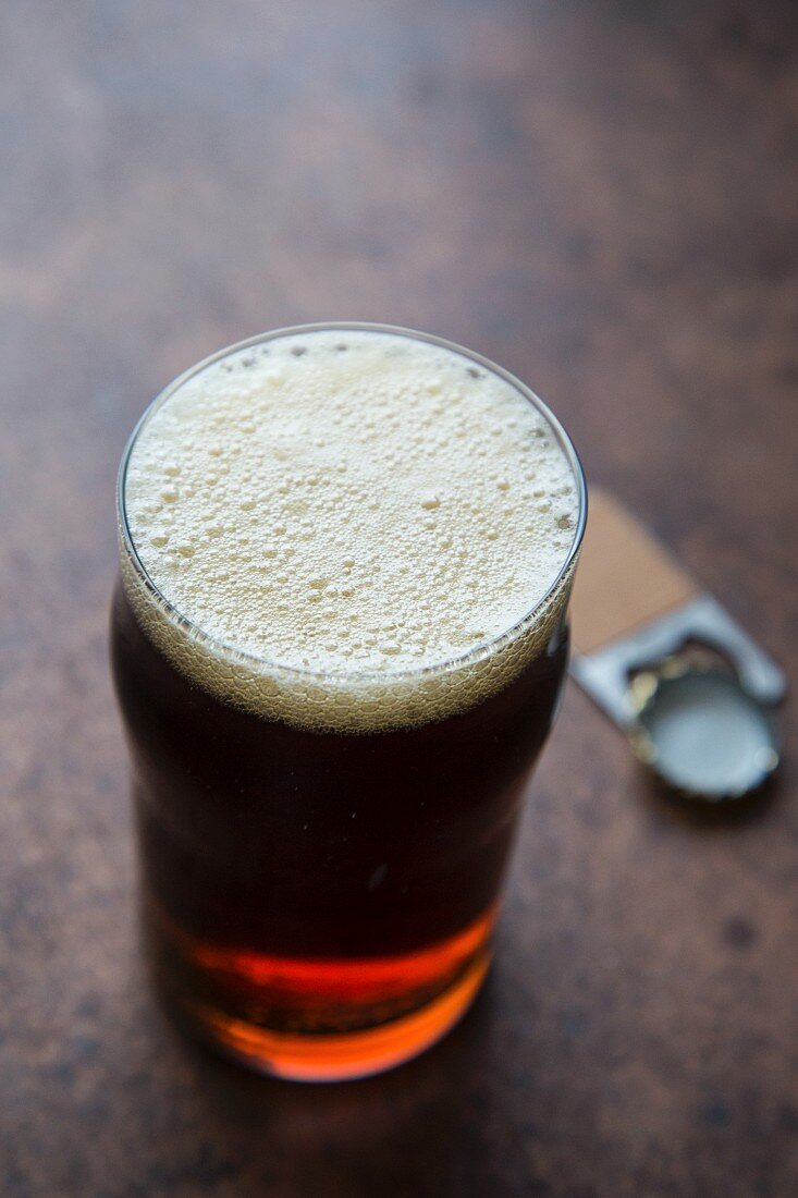 Amber Ale Bier in einem Glas mit Flaschenöffner und Kronkorken