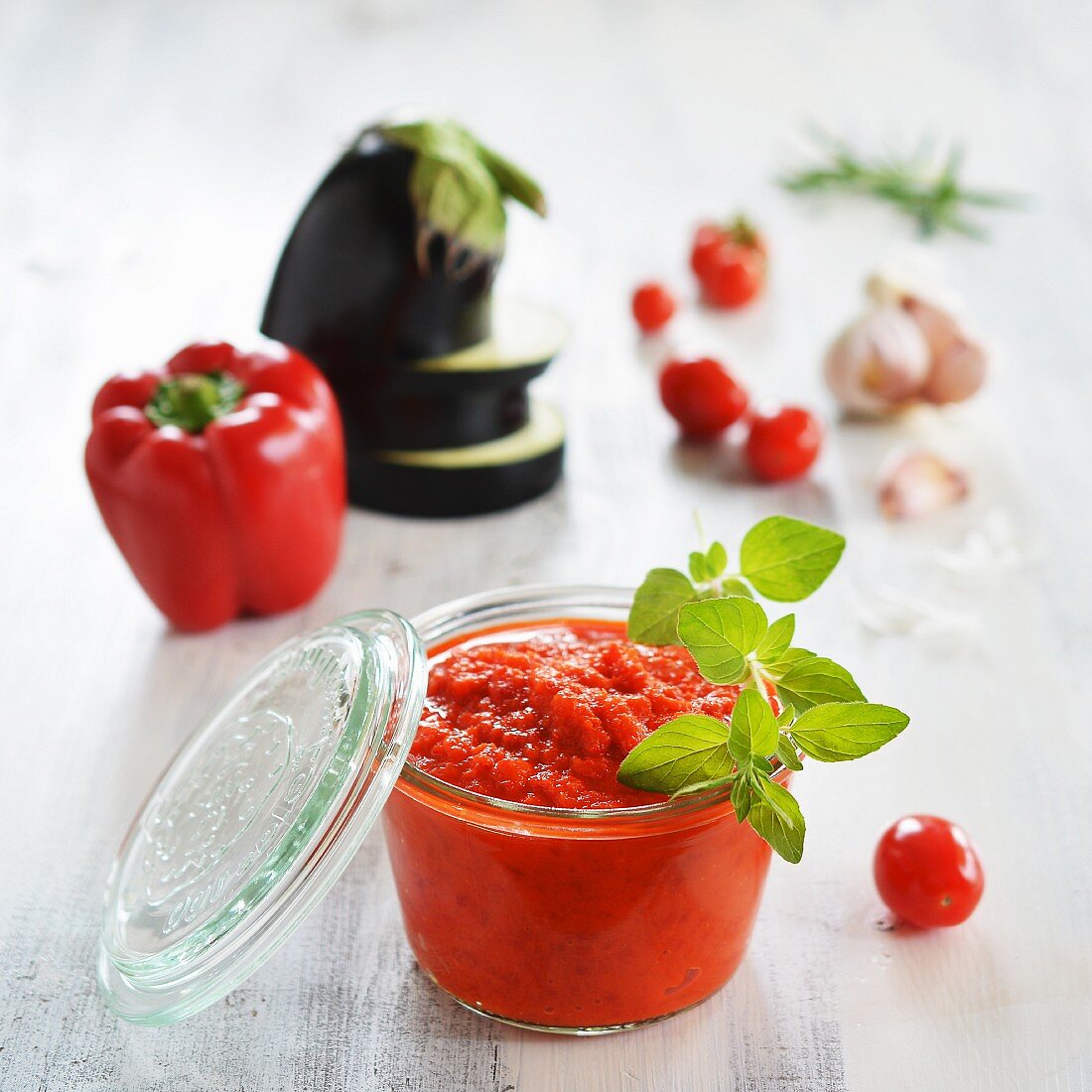 A jar of ajvar and fresh ingredients in the background