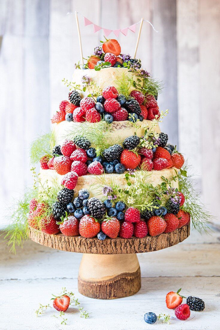 A three tier naked cake with berries on a wooden cake stand