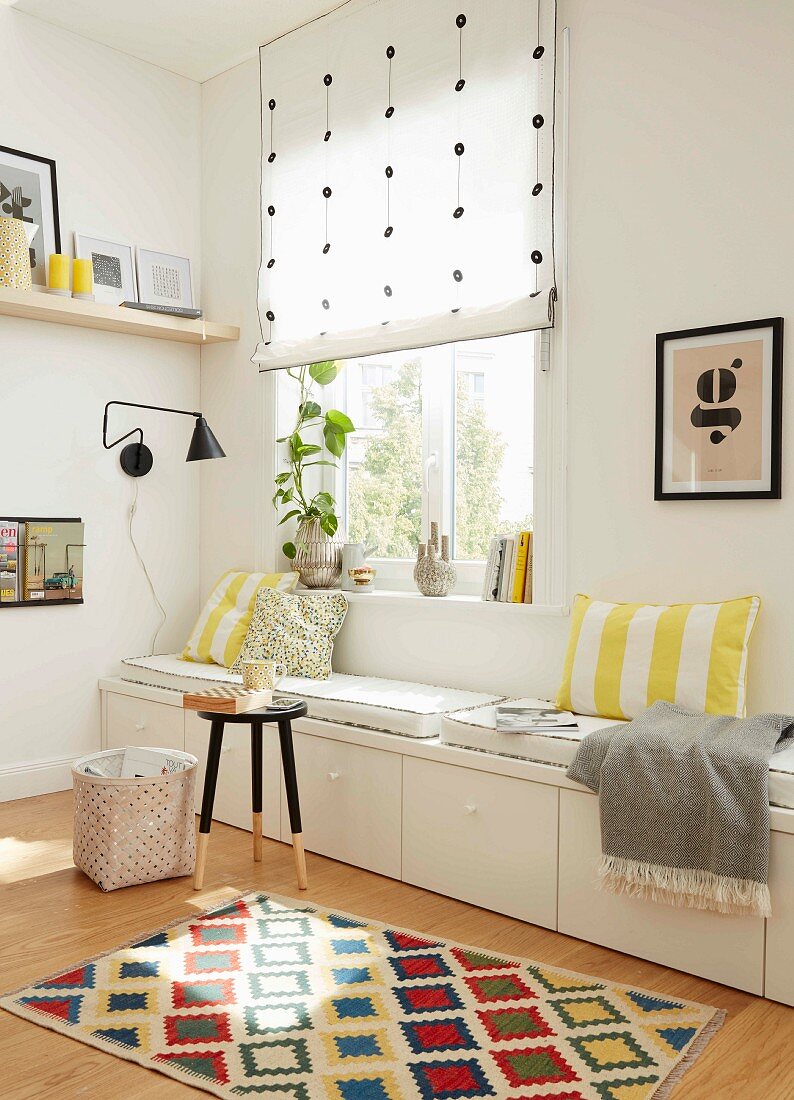 A white, made-to-measure with drawers and cushions in a light corner of a room under a window