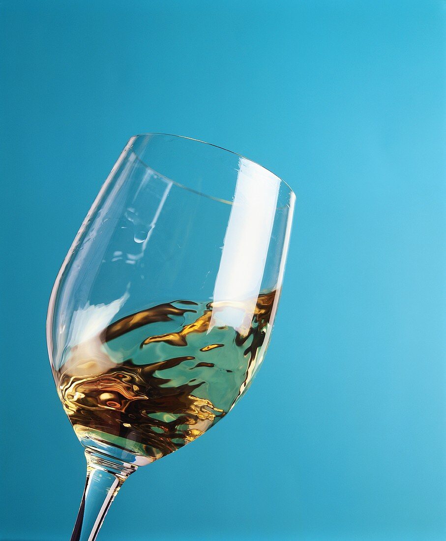 Swirling a glass of white wine against a blue background