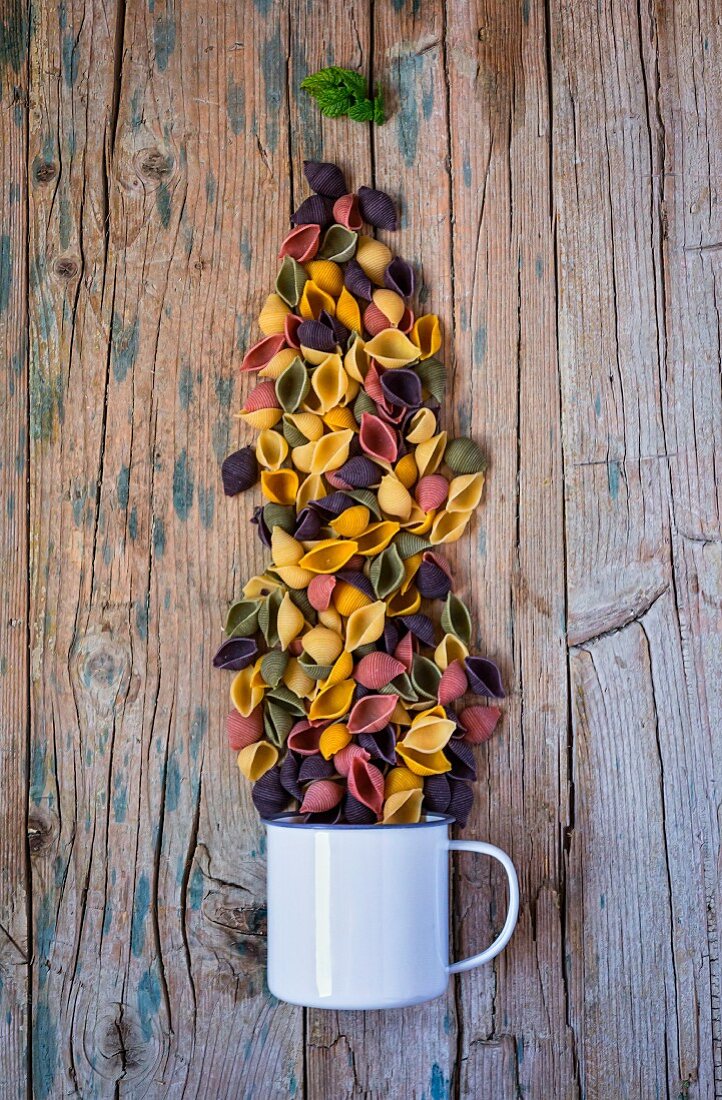 Colourful pasta with an enamel mug on a wooden table