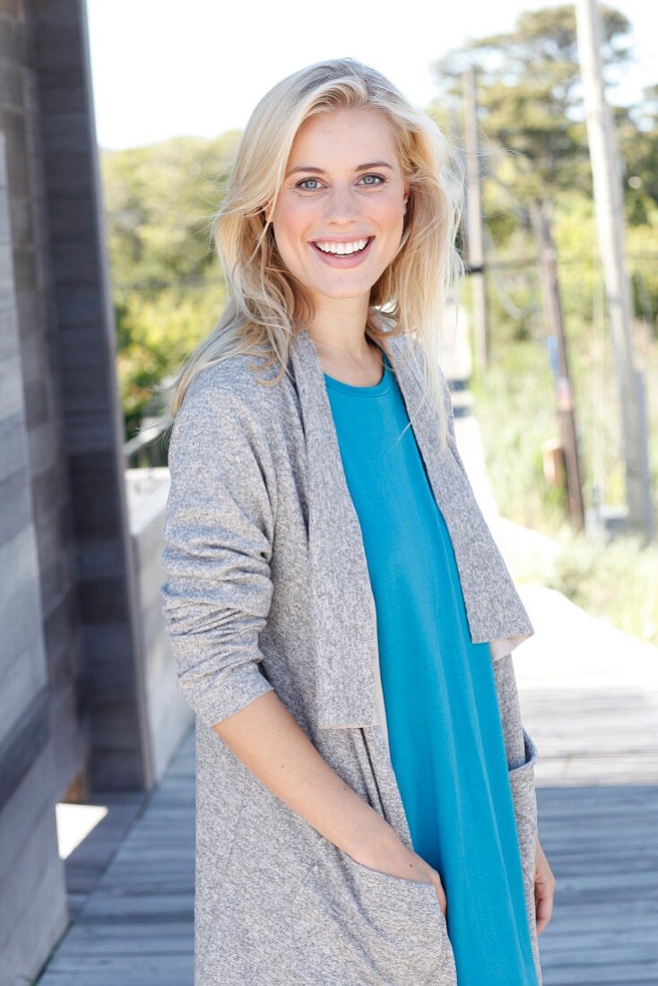 A young blonde woman wearing a blue top and a grey shirt coat