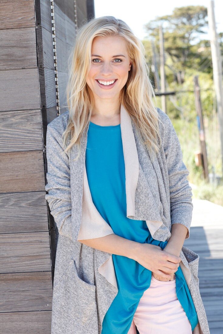 A young blonde woman wearing a blue top and a grey shirt coat