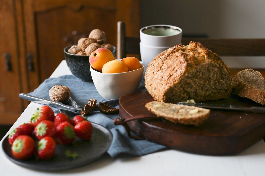 A breakfast table with bread, apricots, strawberries and walnuts