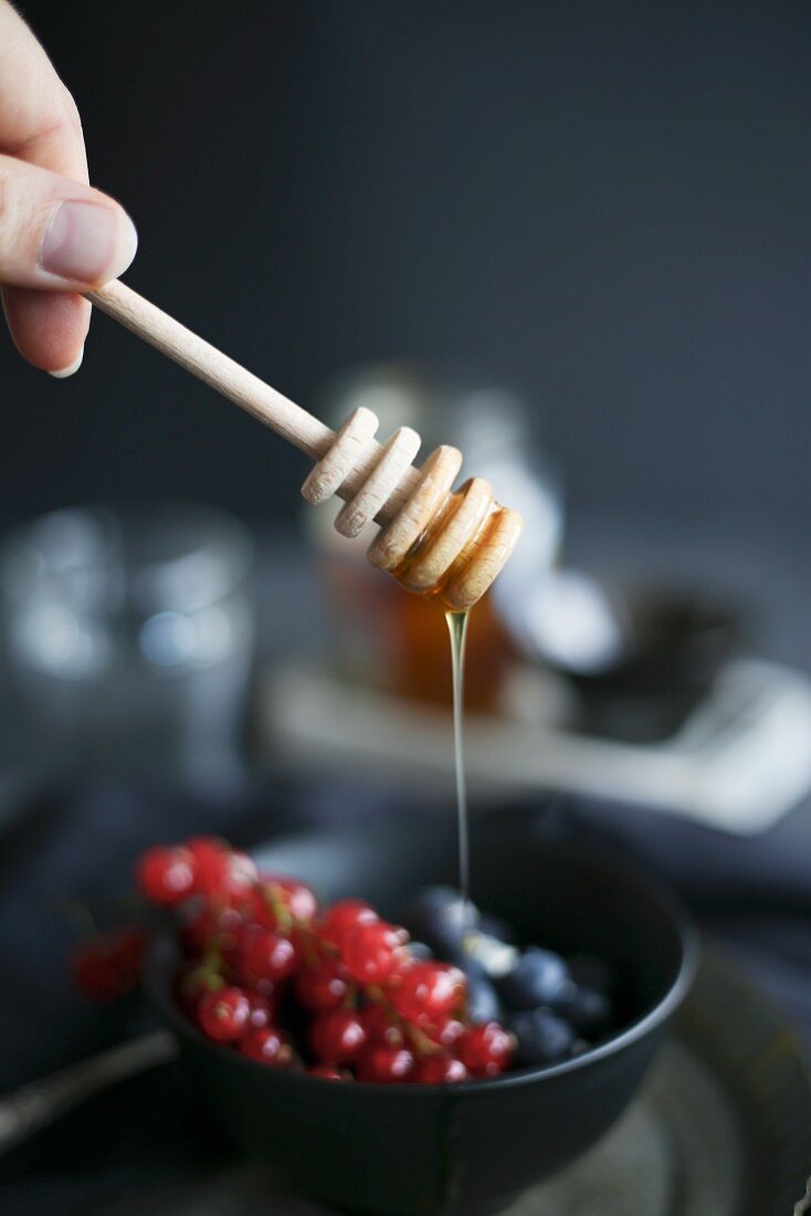 Honey dripping from a dipper onto berries in a dark bowl