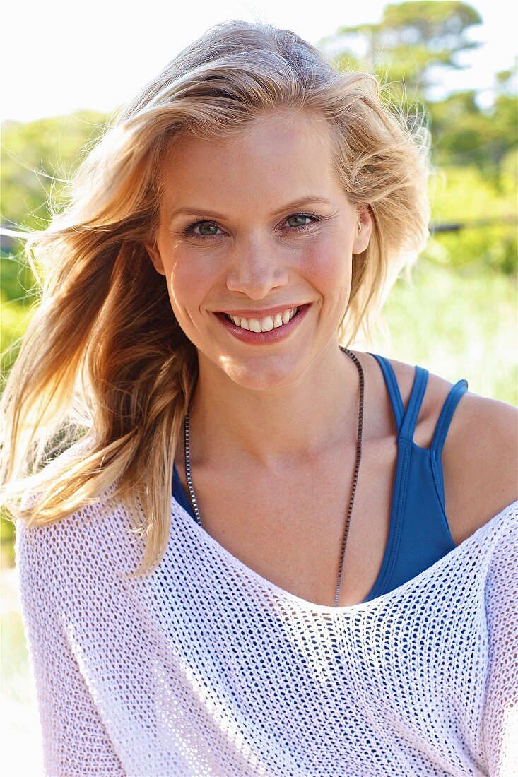 A young blonde woman wearing a blue top and a white net jumper