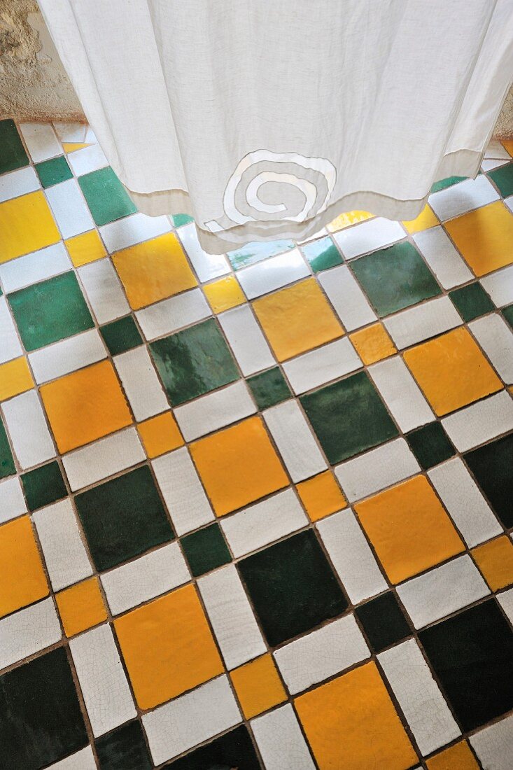 Mehrfarbiger Fliesenboden mit geometrischem Muster und weißer Vorhang mit Spiral-Muster