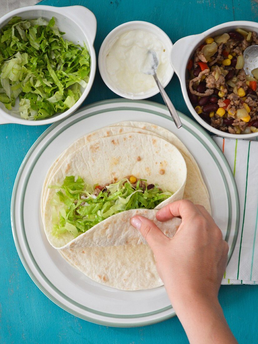 Tortillas being filled with minced meat, sour cream and lettuce