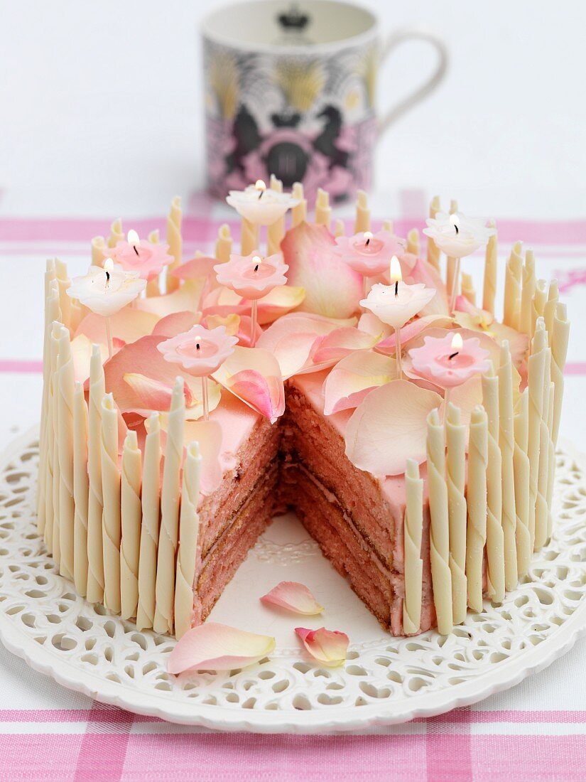 A birthday cake with rose petals, candles and white chocolate