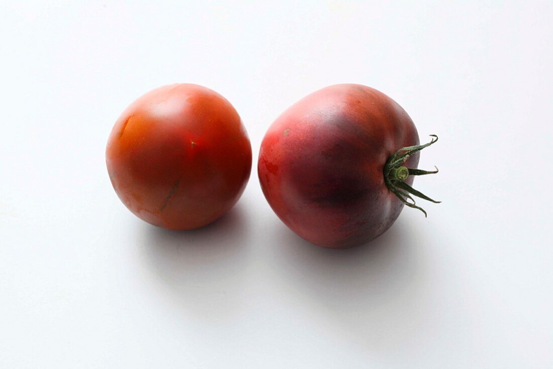 Two black tomatoes on a white surface