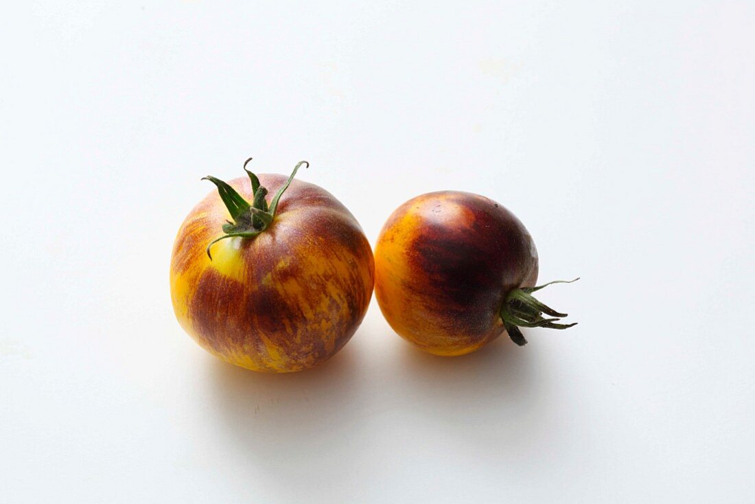 Two yellow-and-black tomatoes on a white surface