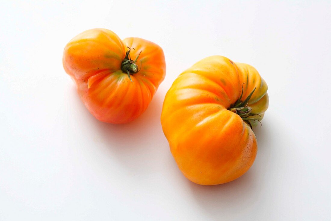 Two yellow beefsteak tomatoes on a white surface