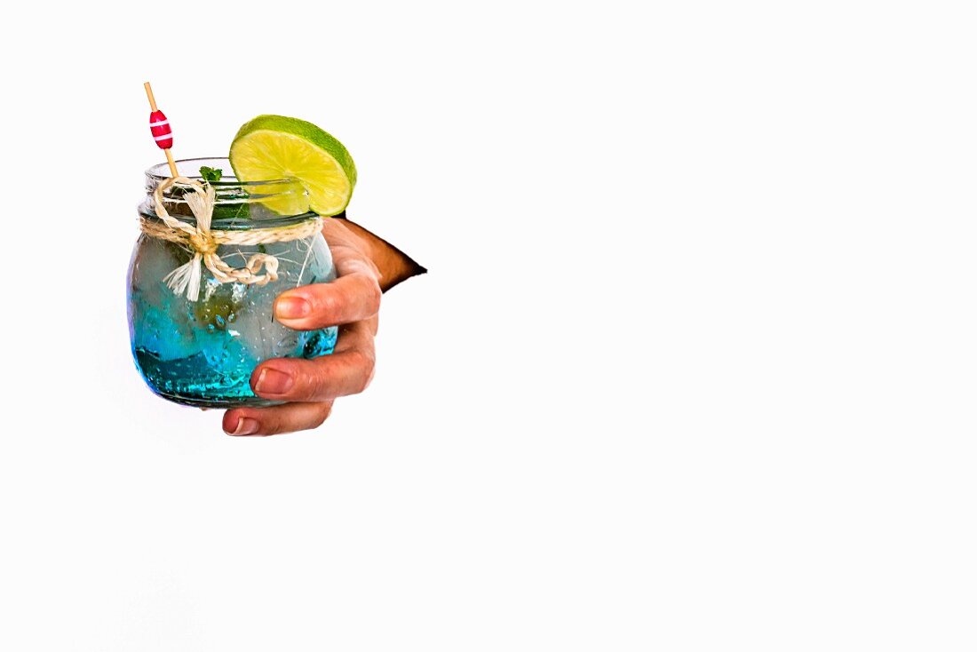 A hand holding a gin and tonic in a preserving jar