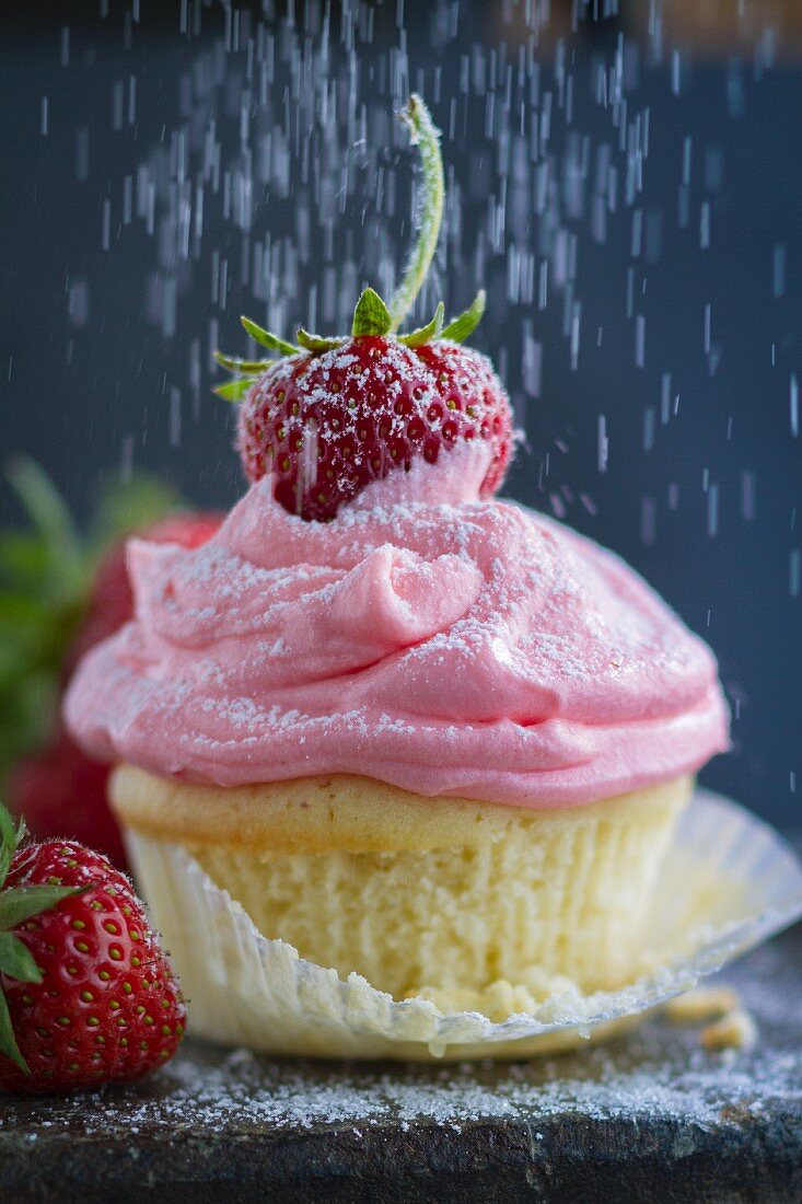 Puderzucker rieselt auf Cupcake mit Erdbeercreme