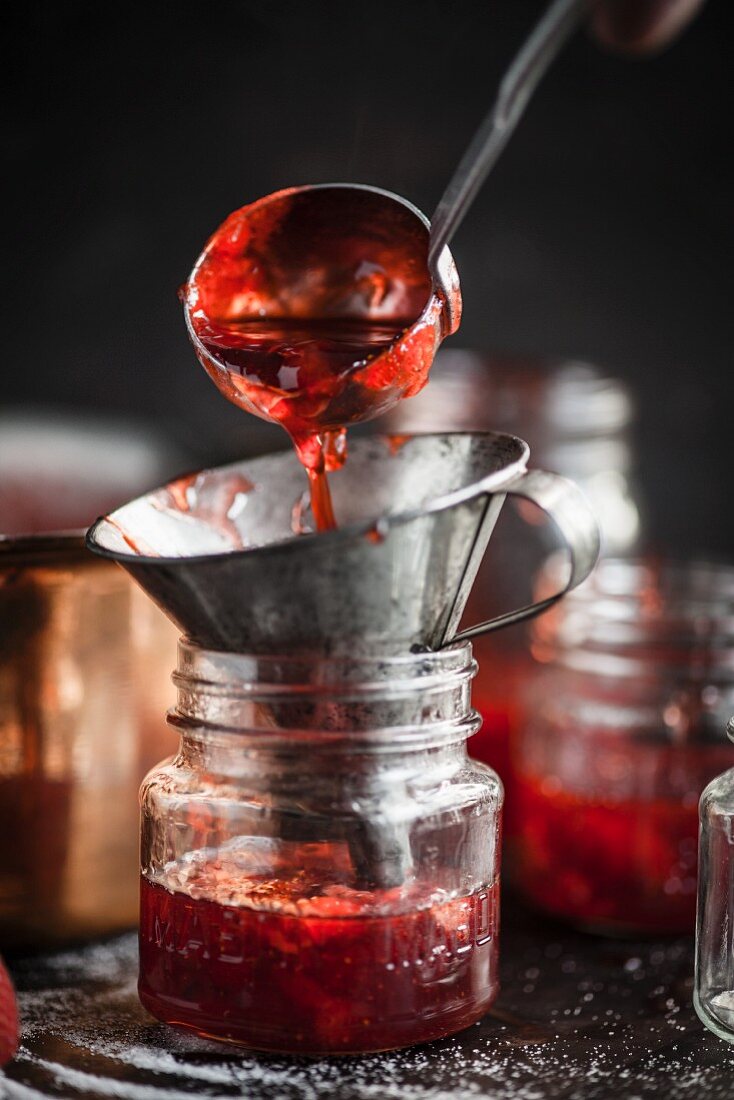 Strawberry jam being filled into a jar with a funnel