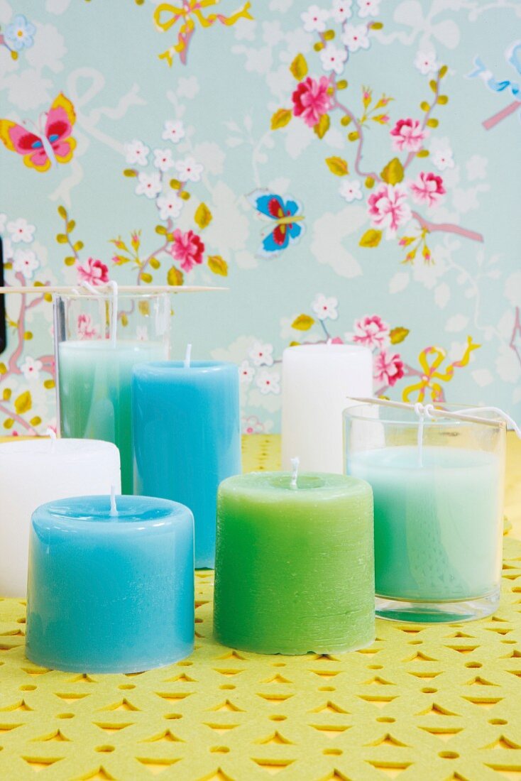 DIY pastel candles poured into drinking glasses against floral wallpaper