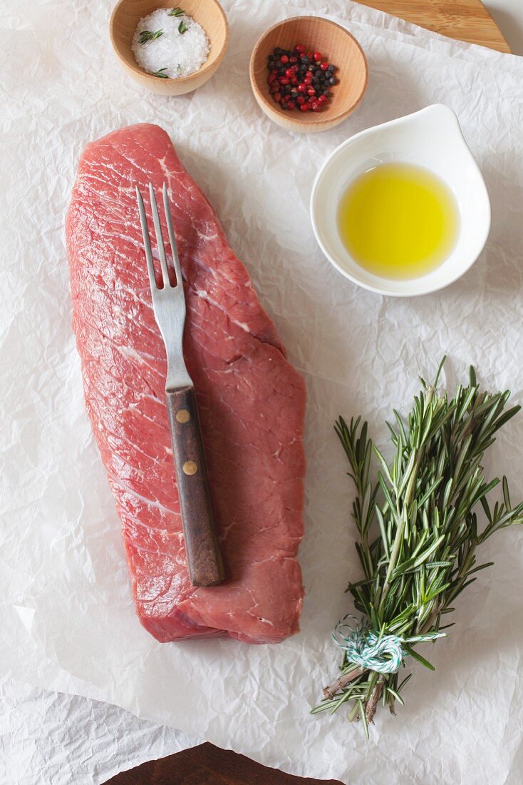 A raw beef steak with spices, oil and rosemary on paper