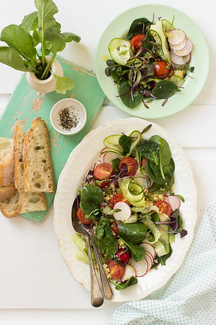 Spinatsalat mit Radieschen, Gurken, Rote-Bete-Blättern, Kirschtomaten, Quinoa, Brot und Pfeffer