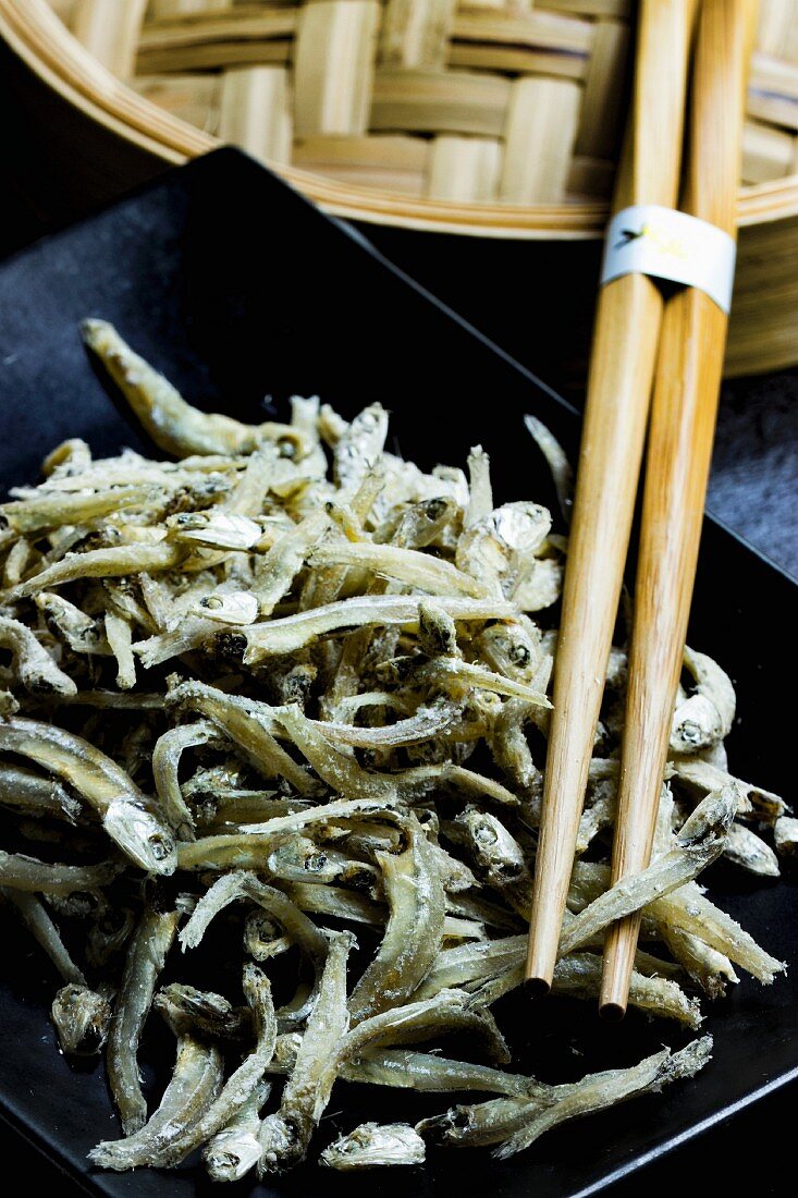 Chirimen (dried Japanese anchovies) with chopsticks and a bamboo steamer on a black plate