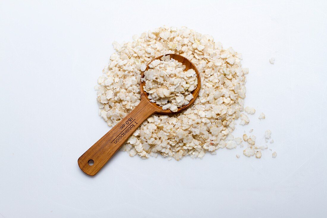 Ein Häufchen Reisflocken mit Holzlöffel vor weißem Hintergrund