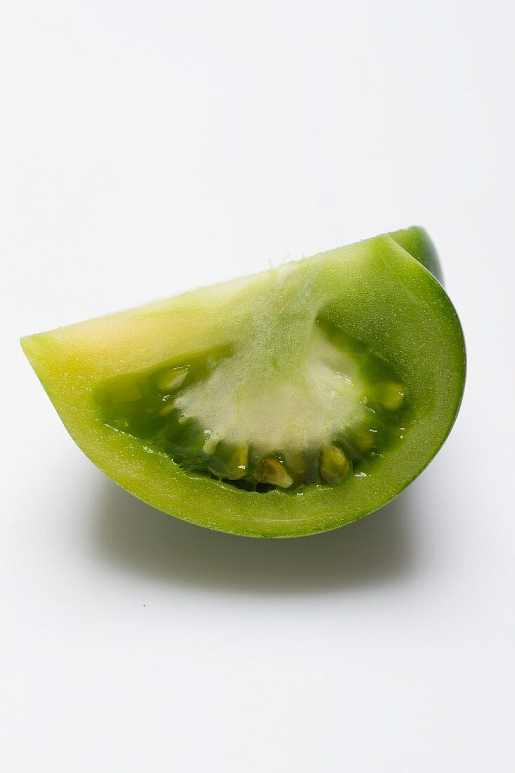 Schnitz einer grünen Tomate vor weißem Hintergrund