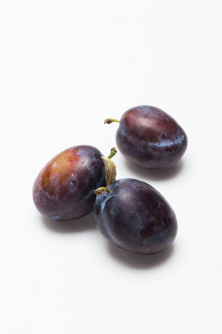 Three damsons on a white surface