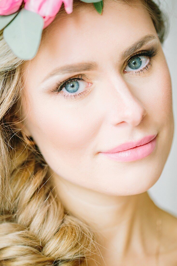 A portrait of a young blonde woman with a fish plait and flowers in her hair