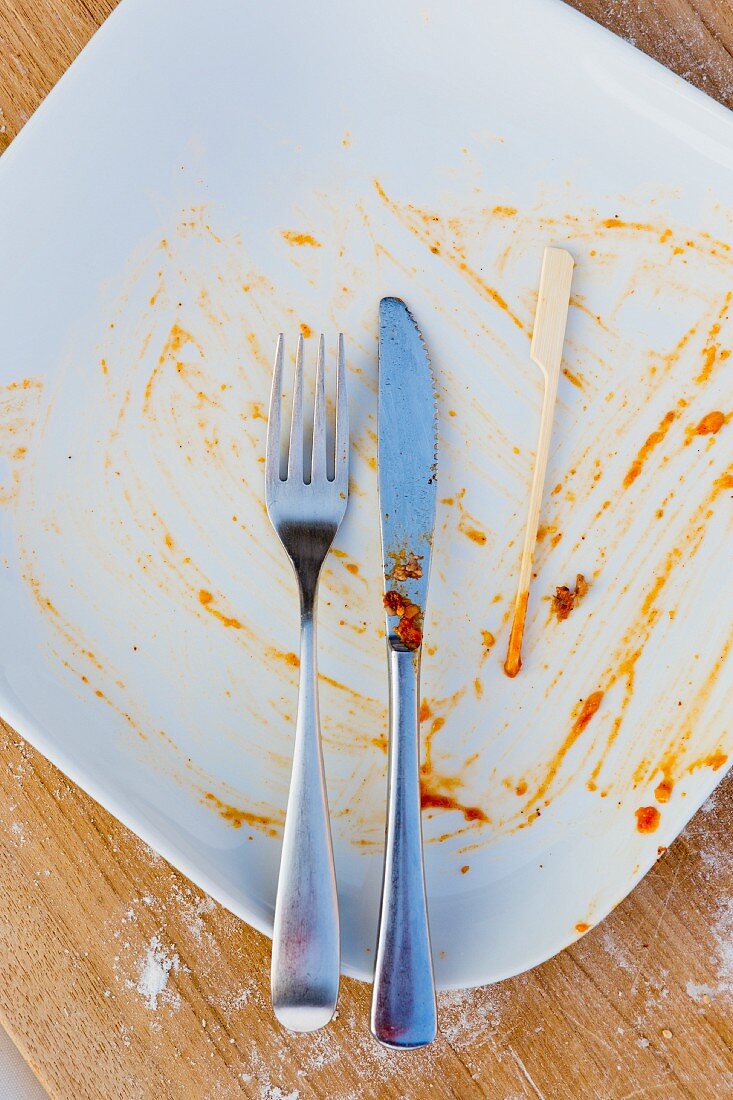 An empty plate with cutlery, a wooden skewer and the remains of sauce