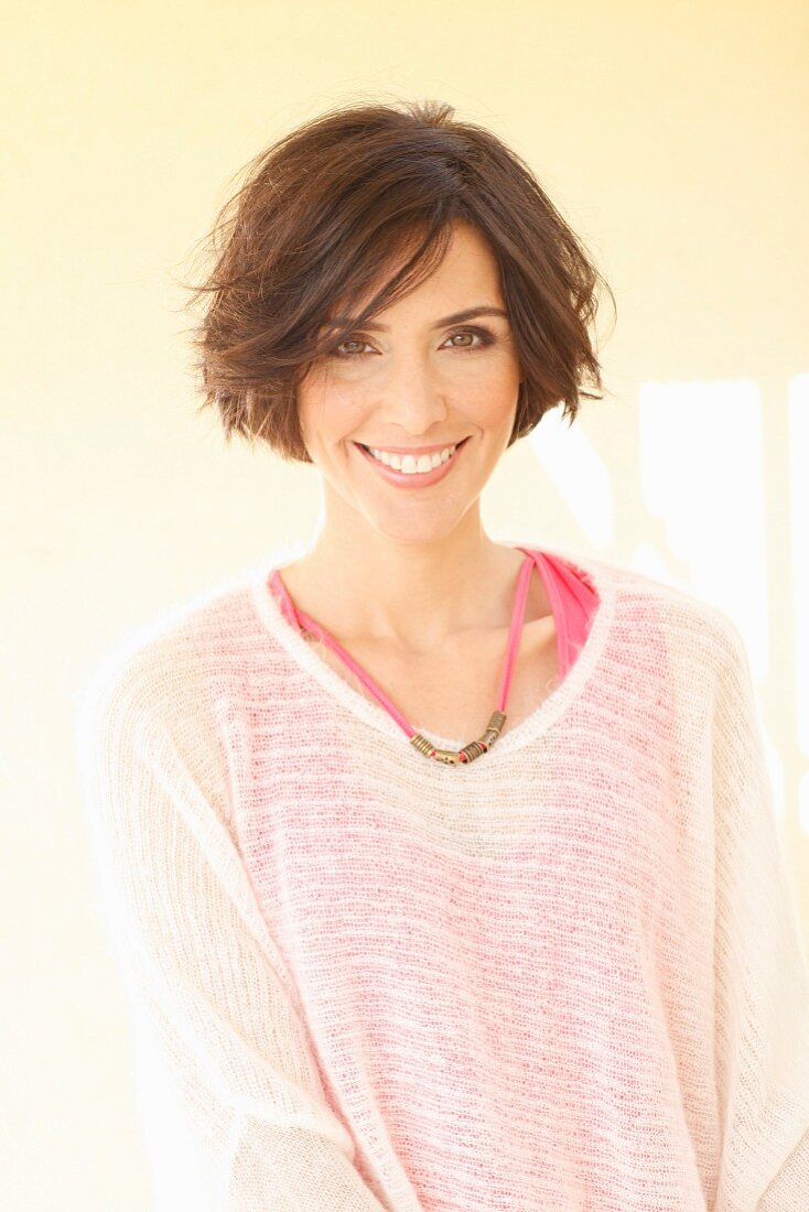 A brunette woman wearing a pink top and a transparent white knitted jumper