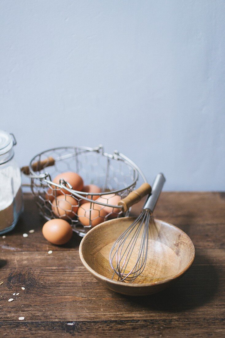an arrangement of eggs in a wire basket and a wooden bowl with a whisk
