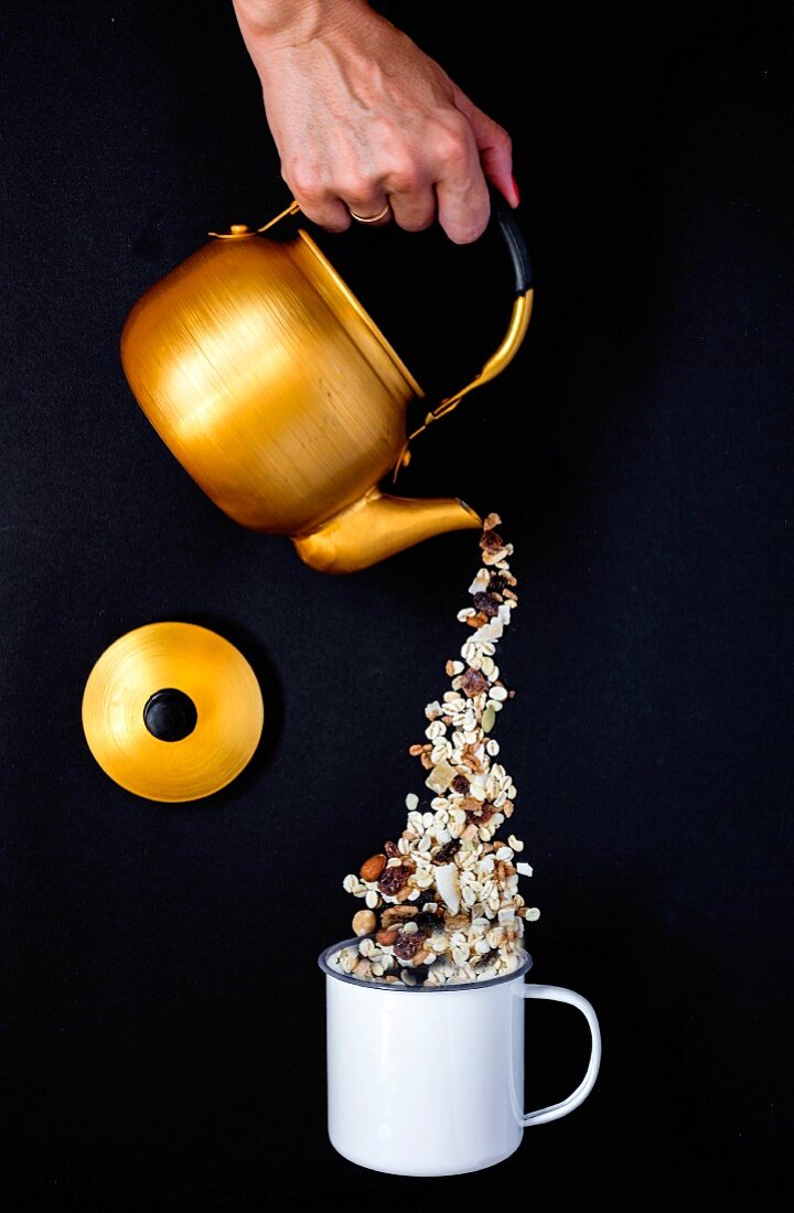 Muesli being poured from a teapot into an enamel mug