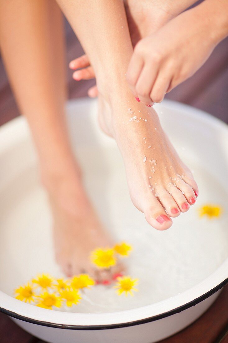 A woman taking a foot bath and having sea salt scrub rubbed into her feet