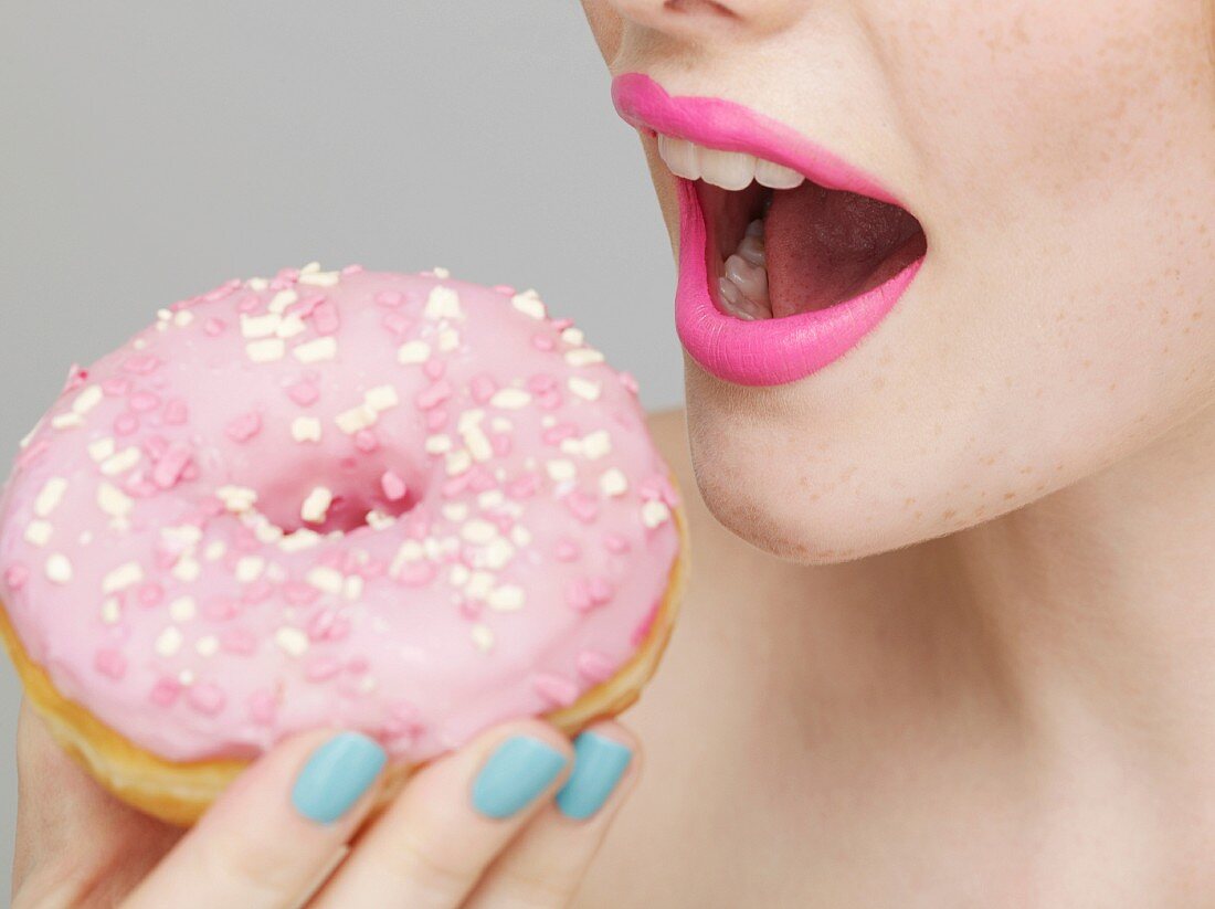 A woman biting into a pink-coloured doughnut