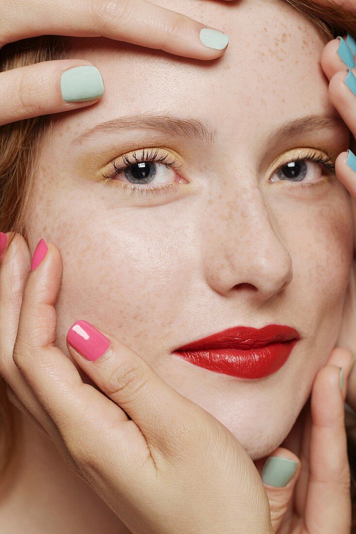 A red-haired woman surrounded by several hands wearing different coloured nail varnishes