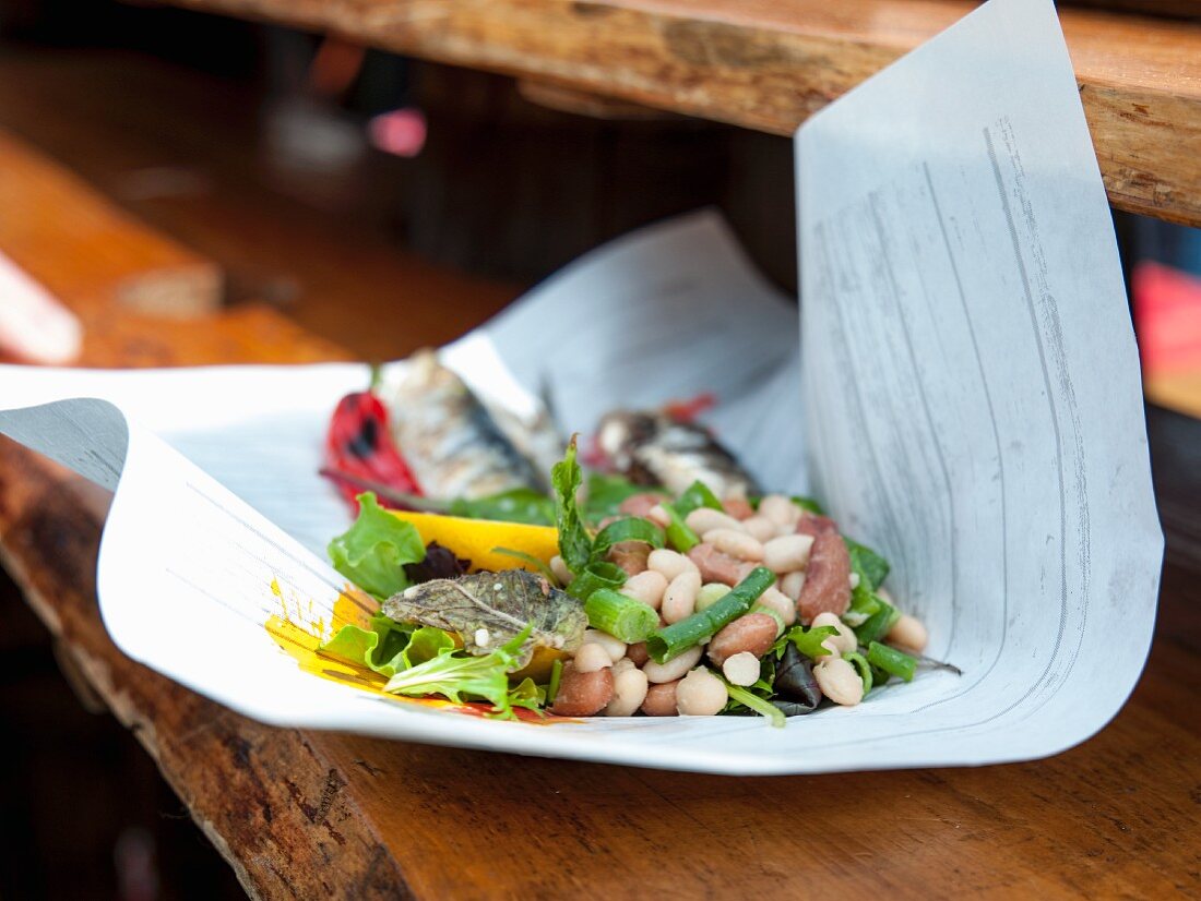 Gegrillte Sardinen und Chilischoten mit Bohnensalat auf Papier (Streetfood)