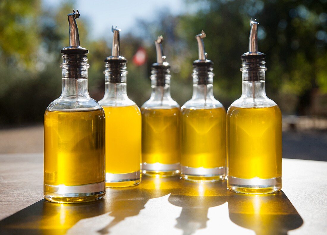 Olivenöl in Flaschen mit Ausgiessern auf Tisch im Freien