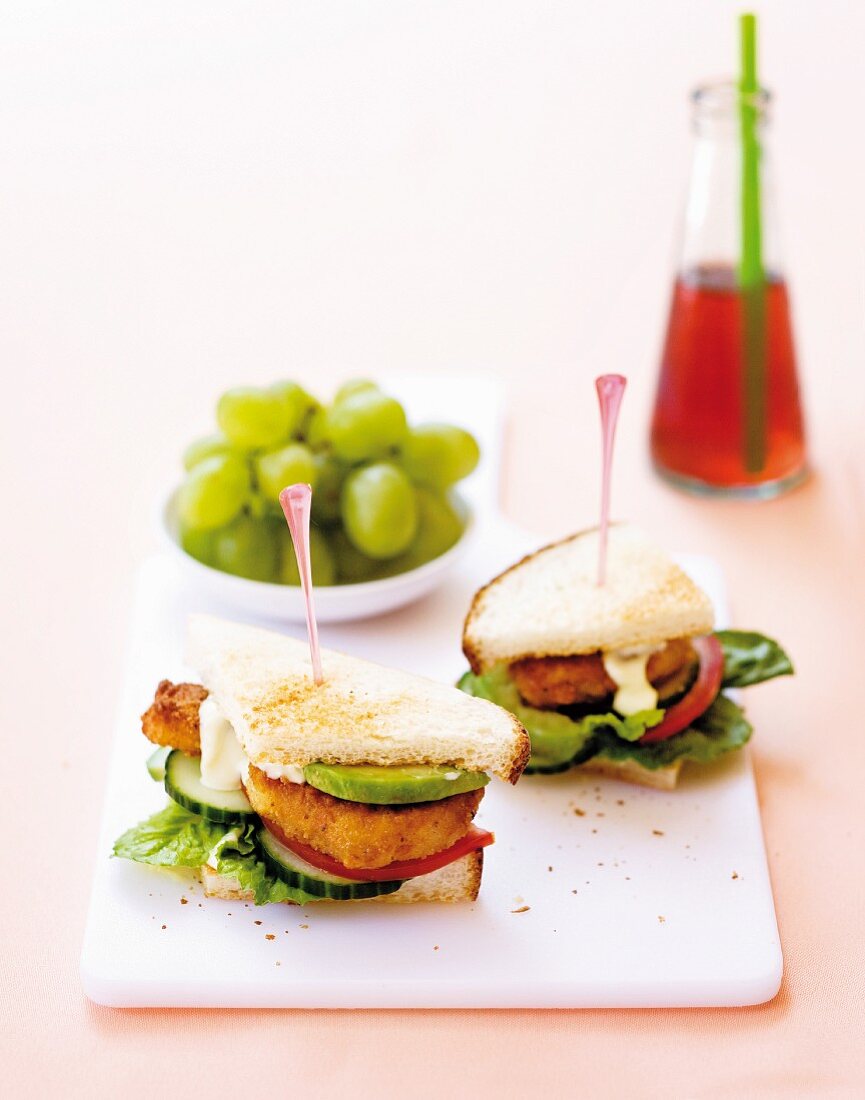 Club sandwiches with chicken nuggets and avocado, grapes in the background